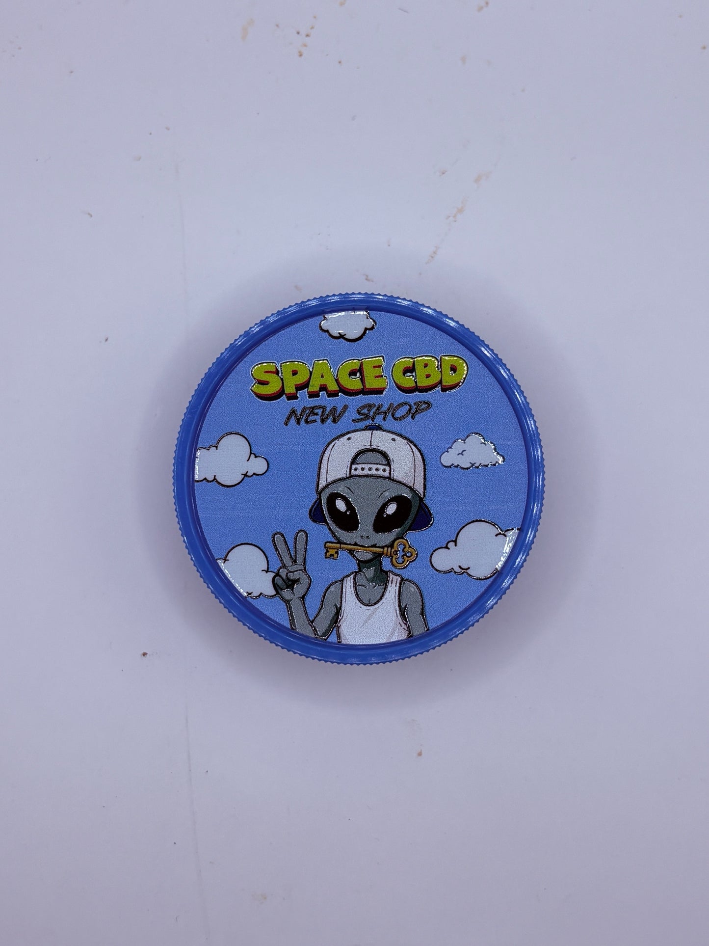 Grinder plastique bleu Space CBD New Shop, alien avec une clé dorée sur fond de nuages